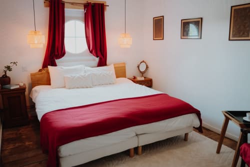 Baccara Lodge bedroom in Arengosse with white bed, red throw, round window, wooden furniture and pendant lights