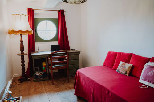 Cozy bedroom at Baccara Lodge with red bed, vintage desk, wooden furnishings and round window