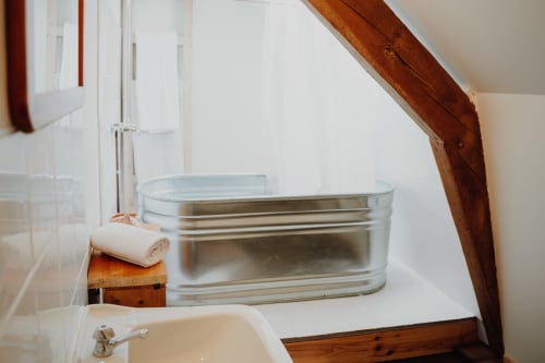Rustic bathroom at Baccara Lodge with galvanized metal bathtub, wooden beams, and white towel in Arengosse