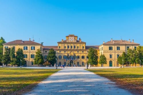 Maestoso palazzo giallo con torre dell'orologio a Parma, circondato da giardini curati e viali alberati