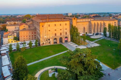Vista aerea del palazzo storico e chiesa di Parma con spazi verdi e skyline cittadino al tramonto