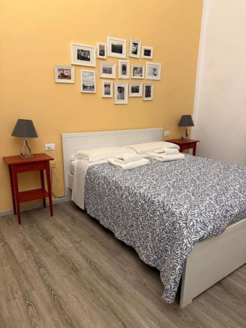 Camera luminosa di Bronze Horse Affittacamere Firenze con letto bianco, piumone decorato, comodini rossi e parete galleria fotografica