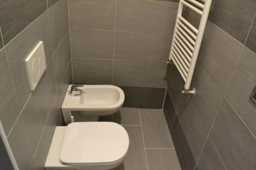 Bagno moderno in Bronze Horse Affittacamere Firenze, con bidet e wc bianchi, pareti in piastrelle grigie e porta asciugamani