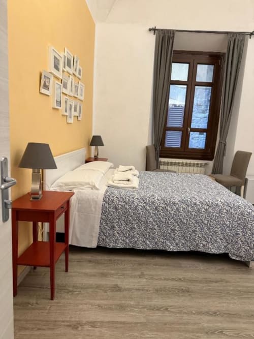 Camera tripla Bronze Horse Firenze con parete gialla, comodino rosso, copriletto a motivi e vista sulla città dalla porta in legno