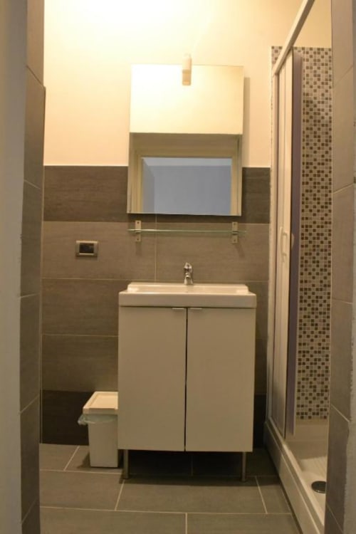 Moderno bagno della struttura B&B a Firenze con vanità bianca, specchio e dettagli in piastrelle marroni