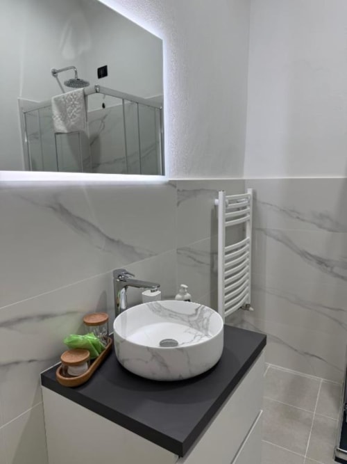 Bagno moderno presso Bronze Horse Affittacamere Firenze con lavabo rotondo in marmo bianco, vanità nera, scaldasalviette e