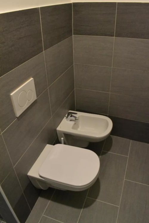 Moderno bagno della Bronze Horse Affittacamere Firenze con bidet e wc bianchi, pareti rivestite in piastrelle scure