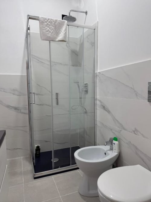 Bagno moderno con cabina doccia in vetro, wc e bidet bianchi, rivestimenti effetto marmo a Bronze Horse Firenze