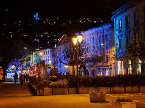 Bellano lakeside piazza at night with blue-lit buildings, holiday decorations, and street lamps