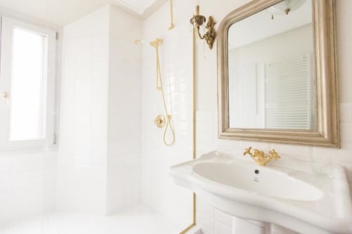 Elegante bagno della Suite 3 presso Alessia's Place a Como, con pareti bianche, lavabo in marmo, rubinetteria dorata e grande specchio incorniciato