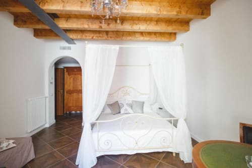 Suite elegante presso Alessia's Place Como con letto a baldacchino bianco, travi in legno a vista e pavimento in cotto.