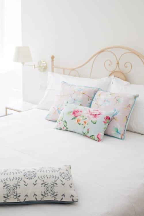 Elegante camera da letto ad Alessia's Place Como con letto in ferro battuto ornamentale, cuscini floreali, biancheria bianca e lampada comodino