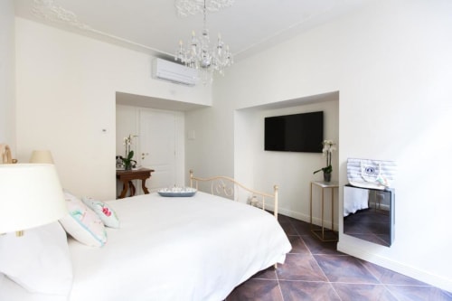 Modern suite bedroom at Alessia's Place Como with white bed, crystal chandelier, wall-mounted TV, and dark tile flooring