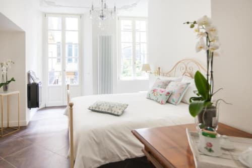 Bright bedroom at Alessia's Place Como with metal bed frame, white linens, floral pillows, potted orchid, and terrace doors