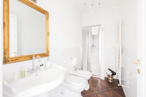 Luxurious bathroom at Alessia's Place Como with gold-framed mirror, white fixtures, and dark tile floor