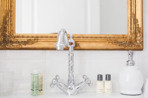 Elegante lavabo da bagno con rubinetto cromato, specchio dorato ornamentale e articoli da toilette presso l'hotel boutique Alessia's Place a Como, Italia