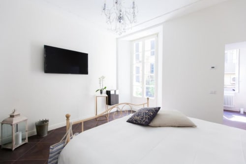 Bright modern bedroom at Alessia's Place in Como with wall-mounted TV, wooden bed frame, white linens, and garden view doors