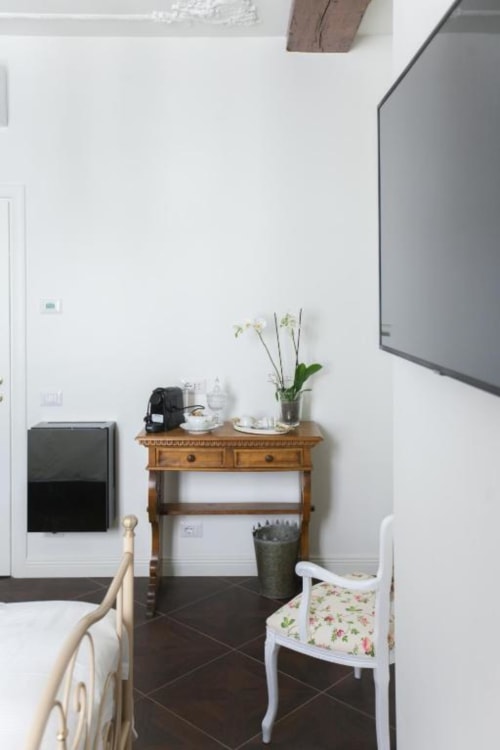 Suite 5 seating area at Alessia's Place Como with wooden desk, white chair, potted orchid, and flat-screen TV on white wall
