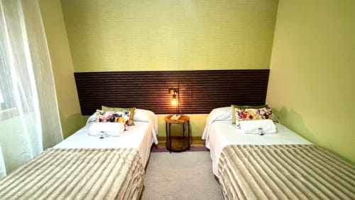 Camas gemelas con mantas rayadas y almohadas decorativas en la habitación de paredes verde brillante del apartamento Holibai Angelitiña