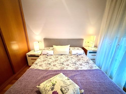 Luminoso dormitorio moderno en apartamento Angelitiña, Baiona con cama doble, cabecero gris, iluminación ambiental y vistas a la ciudad