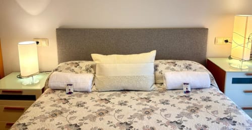 Dormitorio luminoso en apartamento Angelitiña, Baiona con cabecero gris, ropa de cama floral y lámparas modernas de mesita