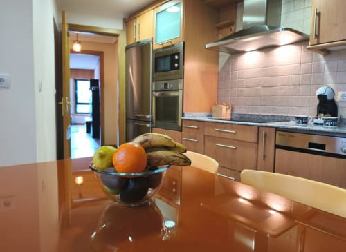 Cocina moderna en apartamento Angelitiña, Baiona con muebles de madera, electrodomésticos de acero inoxidable y frutero en granito