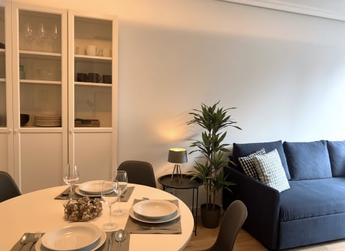 Sala de estar moderna con mesa redonda, sofá azul, planta en maceta y vitrina de cristal en Baiona
