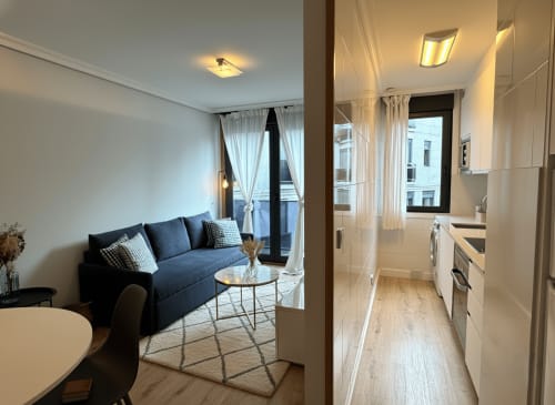 Moderno apartamento Cousiña en Baiona con sofá azul, cocina abierta, muebles blancos y vistas al mar