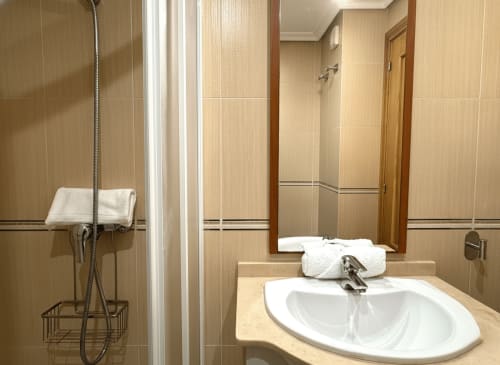 Baño moderno del apartamento Holibai en Baiona con lavabo blanco, espejo, ducha y paredes con azulejos beige