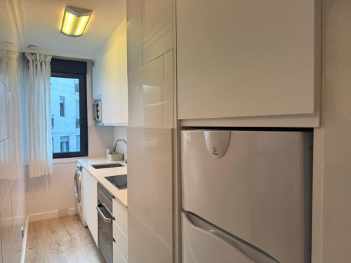 Cocina moderna en apartamento de Baiona con muebles blancos, electrodomésticos de acero inoxidable y ventana con vistas a la calle