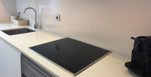 Cocina moderna en apartamento de Baiona con placa de inducción, fregadero y encimeras blancas impecables