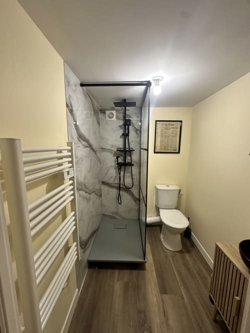 Nowoczesna łazienka w hotelu Lourdes z otwartym prysznicem, toaletą, grzejnikiem do ręczników i żółtymi ścianami