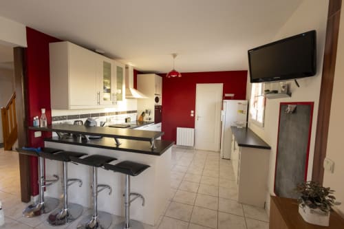 Cuisine moderne avec murs accent rouge, îlot de repas et électroménagers inox au gîte Accolade à Châteaudun