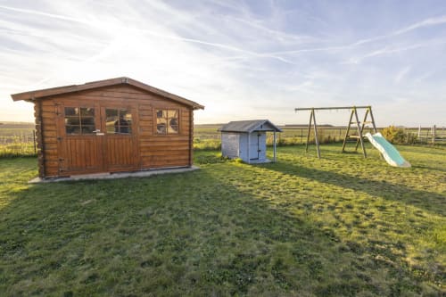 Vue du jardin pittoresque d'Accolade à Châteaudun avec cabanon, cabane de jeu, balançoire et toboggan