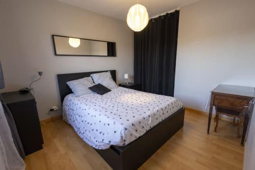 Chambre moderne du gîte Accolade à Châteaudun avec lit à structure noire, oreillers rayés et rideaux vue jardin