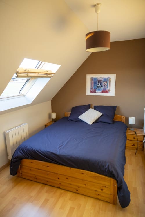 Chambre cosy sous les toits au gîte Accolade à Châteaudun avec lit en bois, linge de lit bleu marine, lucarne et vue sur le jardin
