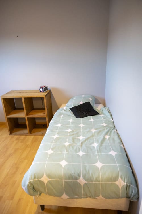 Chambre minimaliste à l'hôtel Accolade avec lit simple, étagères en bois et parquet