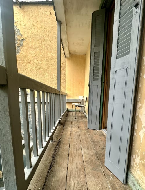Wąski drewniany balkon domku Ombre de la Tour w Lourdes z metalową balustradą i drzwiami do pokoi