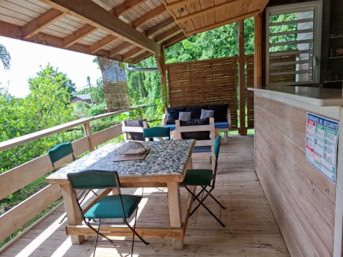 Wooden deck dining area at Le Bougainvillier Blanc bungalow with table, green chairs, lounge seating, and lush tropical views