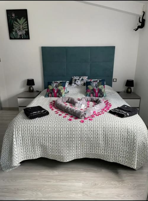 Chambre élégante au Gîte du Miroir avec tête de lit en velours bleu-vert, literie patterned et arrangement romantique de roses roses
