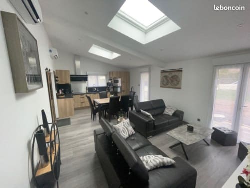 Séjour ouvert et lumineux avec sièges en cuir noir, cuisine bois, puits de lumière et vue sur le jardin au Gîte du Miroir