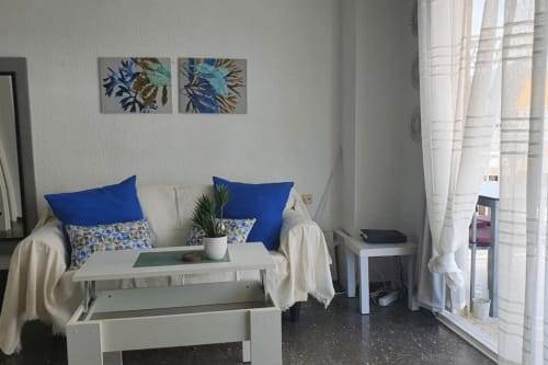 Estudio frente al mar en Benicàssim con sofá blanco, cojines azules, cuadros de mar y terraza con vista al océano con cortinas
