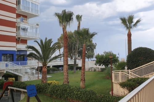 Apartamento frente al mar en Benicàssim con palmeras, jardines cuidados y vistas costeras cerca de edificio a rayas
