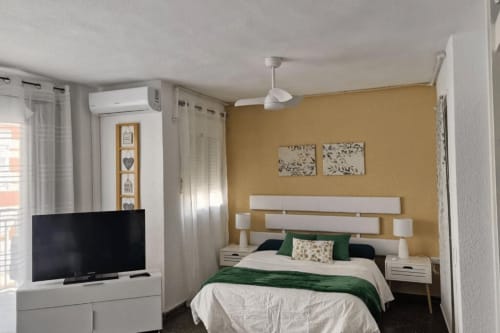 Moderno estudio frente al mar en Benicàssim con cama de acentos verdes, TV y pared con tonos dorados