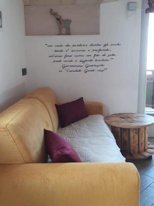 Accogliente living di Al Dos a Livigno: divano dorato, cuscini bordeaux e citazione italiana a muro