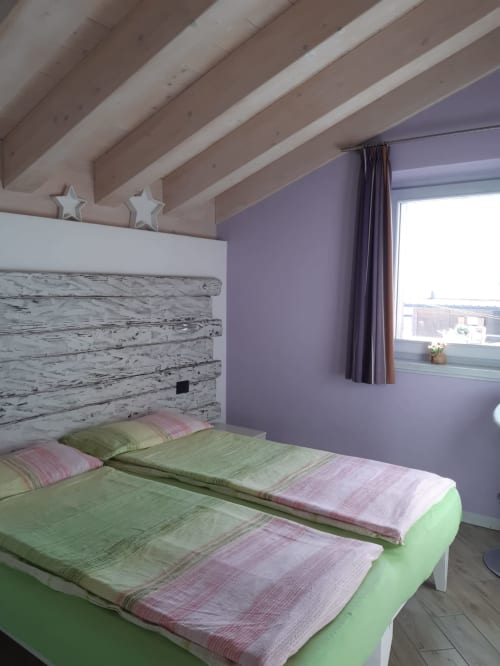 Accogliente camera da letto dell'appartamento di Al Dos a Livigno con pareti viola, testiera in legno bianco e vista sulle montagne