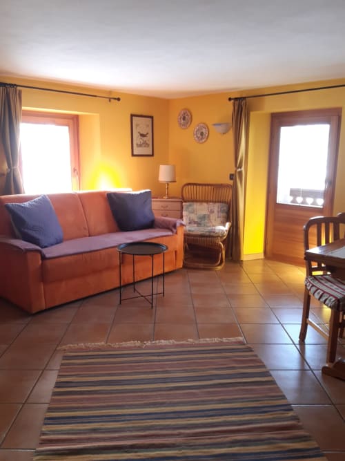 Luminosa zona living dell'appartamento Al Dos a Livigno con pareti arancioni, divano rosso, pavimenti in cotto e vista sulle montagne