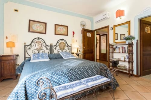 Camera da letto Dormire Assisi con letto in ferro battuto ornato, biancheria blu decorata, piastrelle in terracotta e arredamento tradizionale ad Assisi