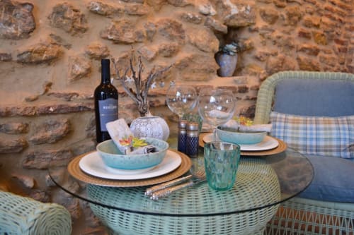 Elegante comedor al aire libre en La Vista Medina Stays con muros de piedra rústica, botella de vino y muebles de mimbre turquesa.