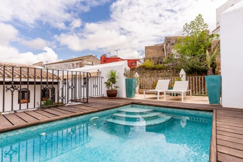Piscina privada color turquesa con terraza de madera, tumbonas blancas y arquitectura andaluza histórica en Casa de